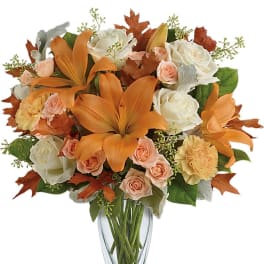 Fall arrangement of orange lilies, peach roses, and white roses in a clear glass vase