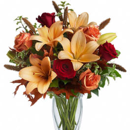 Arrangement of orange lilies and red and orange roses in a clear glass vase