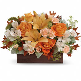 Low rectangular centerpiece with orange lilies, orange and peach roses, and white blooms in a wooden box.