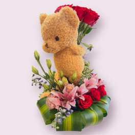 Teddy bear with red roses and pink lilies in a leaf-wrapped base