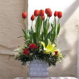 Arrangement of red tulips, roses, and lilies in a white vase