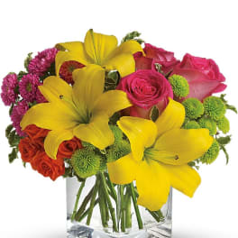 Bright mix of yellow lilies, pink roses, and green mums in a clear glass cube vase