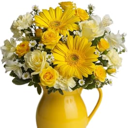 Yellow and white flower arrangement with gerbera daisies and roses in a yellow ceramic pitcher