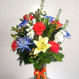Mixed bouquet of roses, lilies, and blue daisies in a glass vase