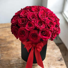 Red roses arranged in a black hatbox with a red ribbon