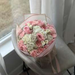 Pink and white bouquet of roses, hydrangeas, and carnations wrapped in pale pink paper