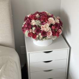 Round bouquet of pink and burgundy roses with small white filler flowers in a white box