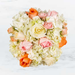 Round bouquet of cream, pink, and orange roses with pale hydrangeas