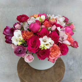 Mixed pink, white, and orange flowers arranged in a white vase