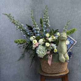 Basket arrangement with blue and white flowers and a plush dinosaur