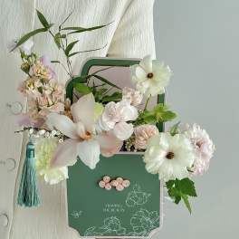 Pastel floral arrangement in a decorative green box with a tassel