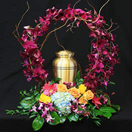 Floral urn arrangement with magenta orchids, roses, and hydrangea around a gold urn
