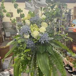 Tall floral standing spray with white roses and blue flowers on an easel