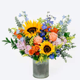 Mixed bouquet with sunflowers, roses, and blue flowers in a metal vase