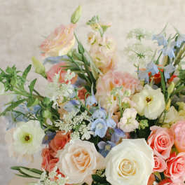 Pastel bouquet of roses, blue flowers, and white blooms in a white vase