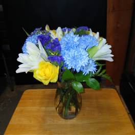 Mixed bouquet of blue, white, yellow, and purple flowers in a glass vase