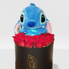 Blue plush toy sitting above a cluster of red roses in a black hat box