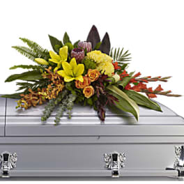 Floral spray on a silver casket with yellow lilies and orange roses