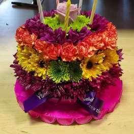 Colorful tiered flower cake with candles on a pink base