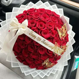 Round bouquet of red roses with a white ribbon and decorative butterflies