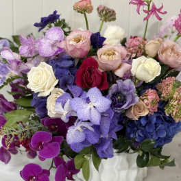 Mixed bouquet of roses, orchids, and hydrangeas in a white vase