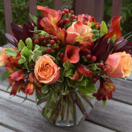 Peach roses and red-orange flowers arranged in a clear glass vase