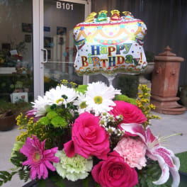 Birthday balloon above a colorful flower arrangement in a basket