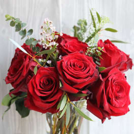 Arrangement of red roses with small white filler flowers in a clear glass vase