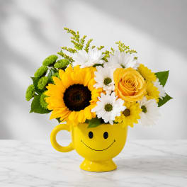 Bouquet of sunflowers, daisies, and a yellow rose in a smiley-face mug
