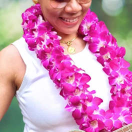 Woman wearing a bright pink orchid lei and holding a guitar