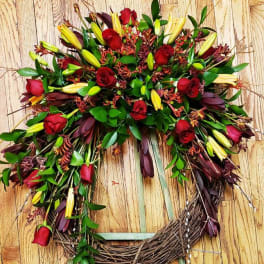 Heart-shaped wreath with red roses and yellow lilies on a wooden background