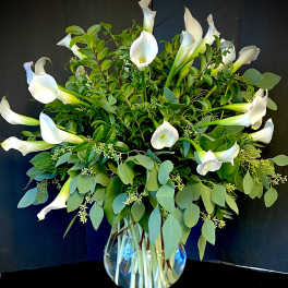 White calla lilies in a clear glass vase with lush greenery