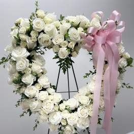 Heart-shaped white rose wreath with a pink ribbon on a stand