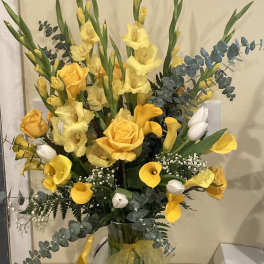 Yellow flowers and roses arranged in a clear glass vase
