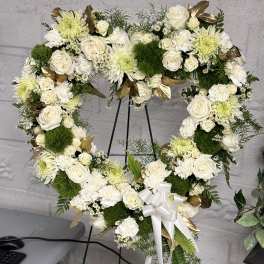 Heart-shaped white floral wreath on an easel with a ribbon bow
