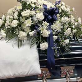 White floral casket spray with a navy ribbon on a black casket