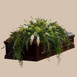 Green and white floral casket spray on a dark wood coffin