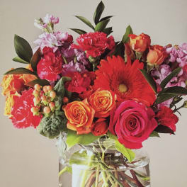 Mixed bouquet of red, orange, and pink flowers in a clear glass vase
