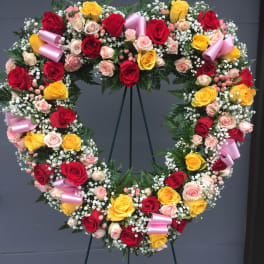 Heart-shaped wreath of red, yellow, and pink roses with ribbon accents