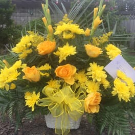 Yellow and orange flowers arranged in a white container with a yellow bow.