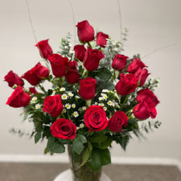 Red roses arranged in a clear glass vase with small white filler flowers