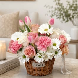 Pink and white flowers arranged in a wicker basket on a table
