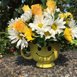 Yellow mug with a smiley face holding white daisies and yellow roses