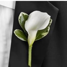 White calla lily boutonniere with green leaves on a black suit lapel