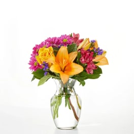 Bouquet of orange lilies, yellow roses, and pink daisies in a clear glass vase