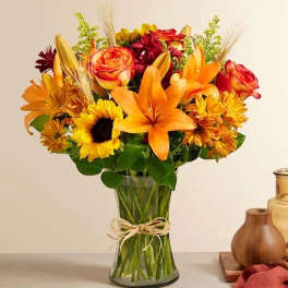 Bouquet of orange lilies, roses, and sunflowers in a glass vase