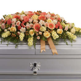 Large floral spray on a silver casket with peach and yellow blooms
