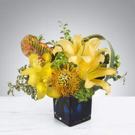 Yellow lilies and orchids arranged in a blue glass vase