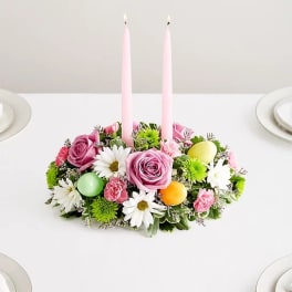Pink floral centerpiece with two tall candles on a white table
