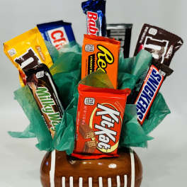 Candy bars arranged in a football-shaped ceramic container with green tissue paper